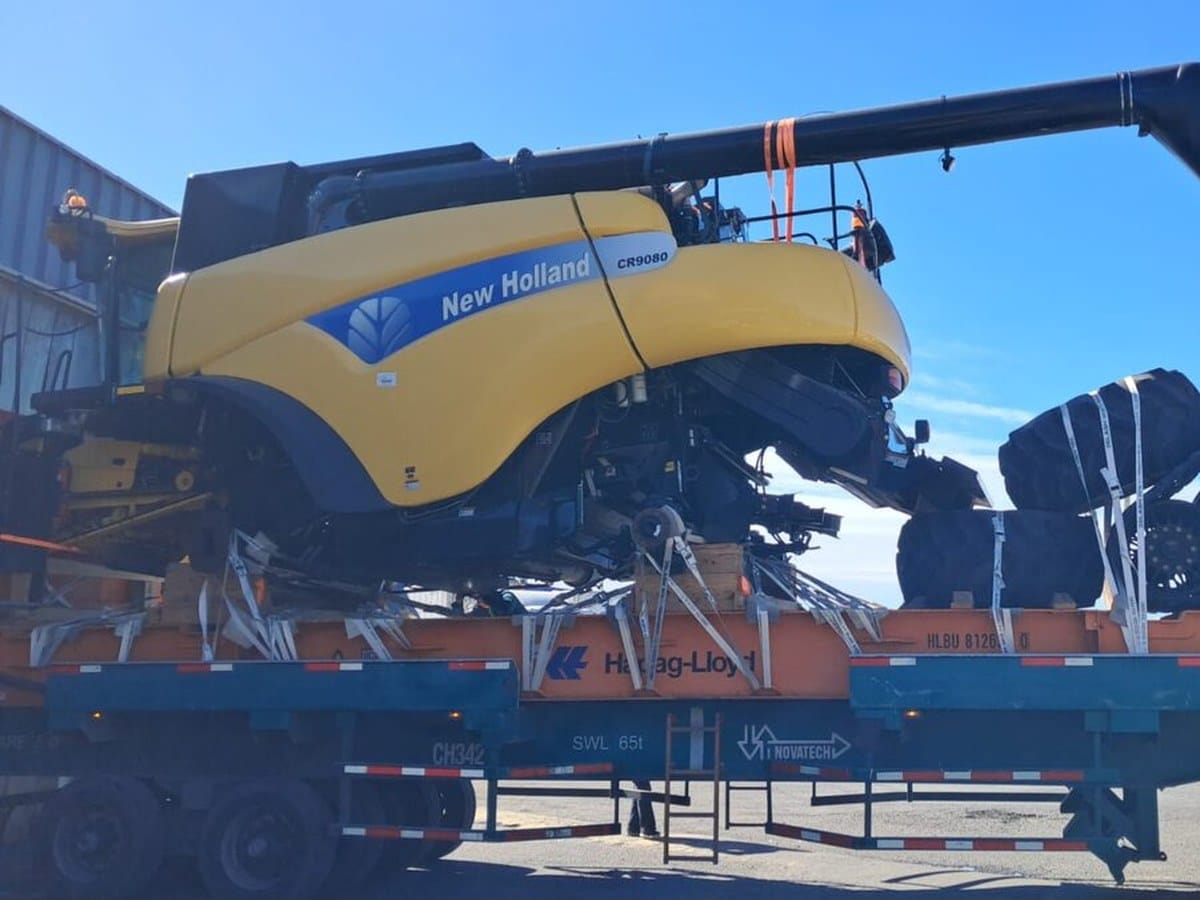 New Holland CR9080 combine, yellow, lashed to a flat rack on timber blocking, large black components strapped beside it
