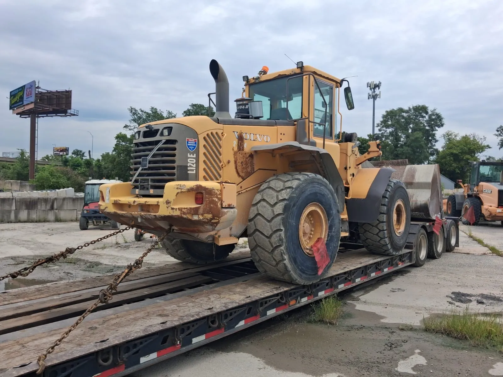 Front of the Volvo L120E with its cab, exhaust stack and red-flagged wheels on a chained lowboy deck